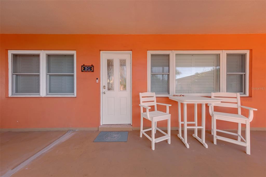 An orange exterior wall features a white door, windows, and a small patio furniture set — 121 46TH AVENUE UNIT 2G, ST PETE BEACH, FL