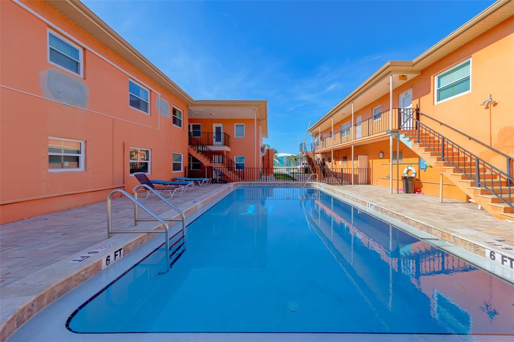 A rectangular swimming pool sits between two orange apartment buildings with exterior staircases — 121 46TH AVENUE UNIT 2G, ST PETE BEACH, FL