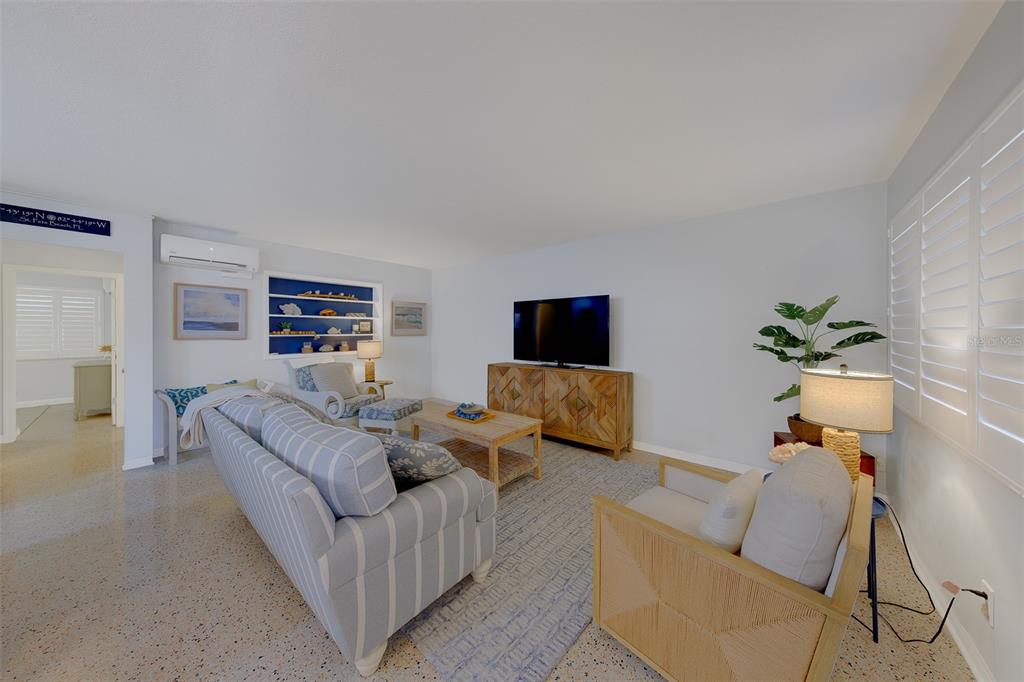 A living room features a striped sofa, a wooden media console, and a blue-backed shelving unit — 121 46TH AVENUE UNIT 2G, ST PETE BEACH, FL