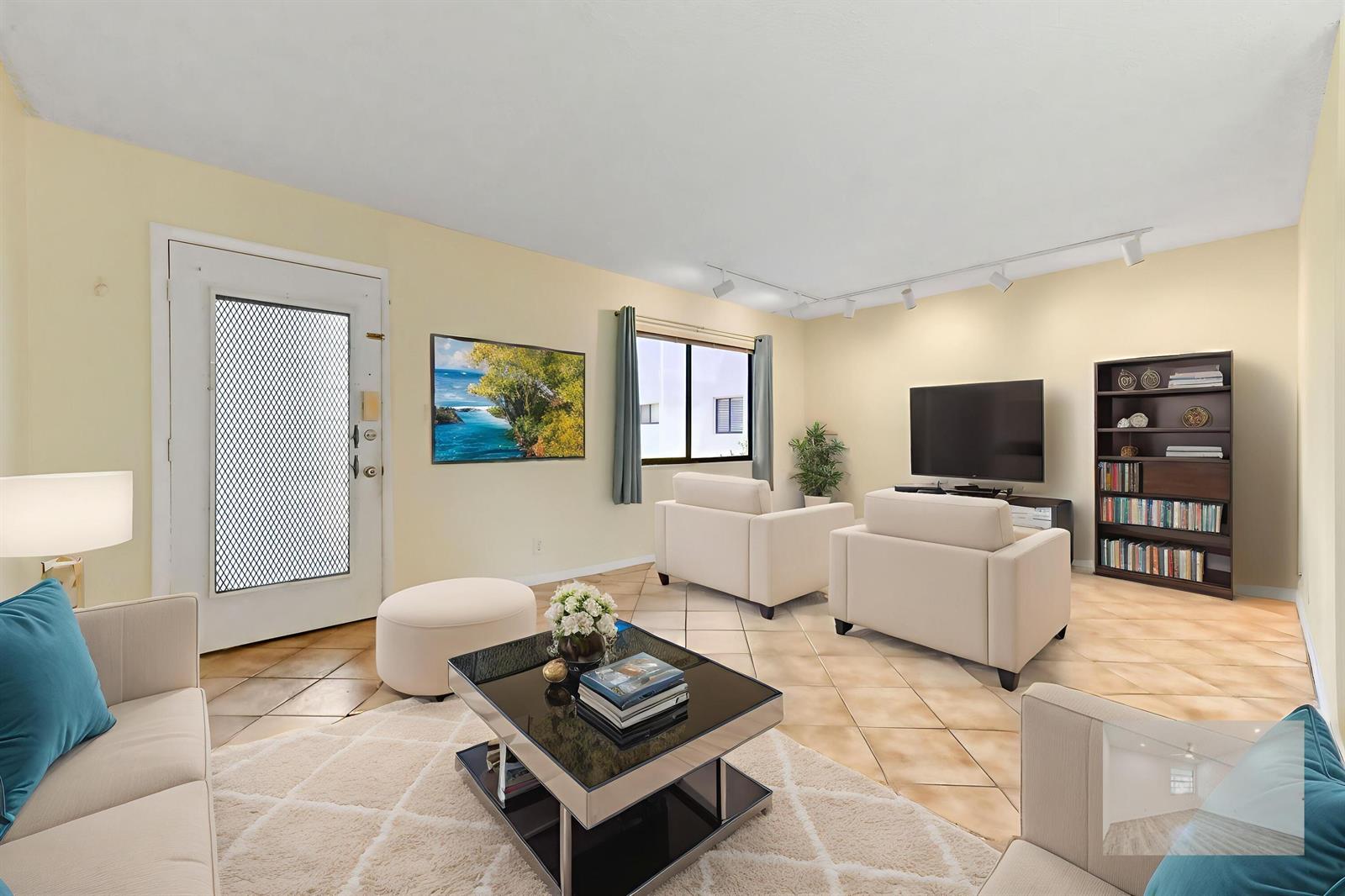 A living room features light-colored walls, tile flooring, two armchairs, a television, and shelving — 15054 Ashland Way # 84, Delray Beach FL 33484, DELRAY BEACH, FL
