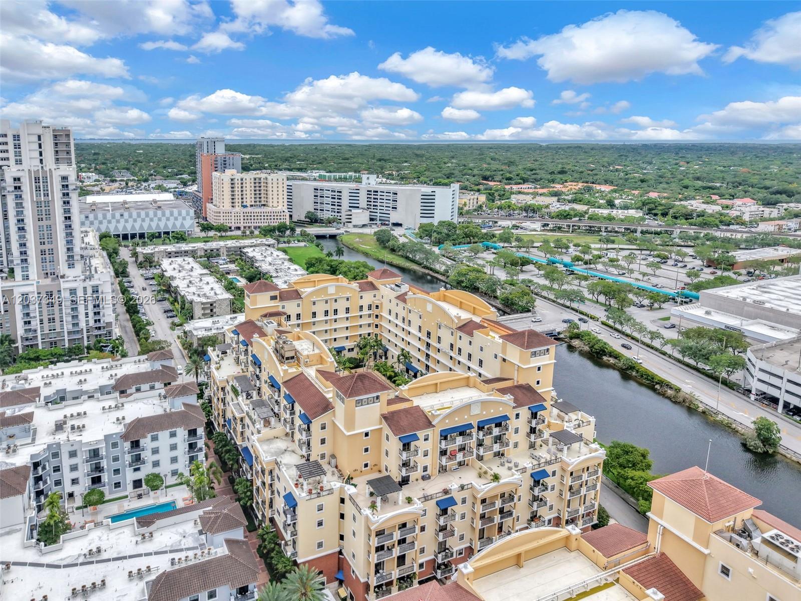 An aerial view shows a large, multi-story yellow apartment complex situated beside a canal — 8390 SW 72nd Ave # 905, Miami FL 33143, MIAMI, FL