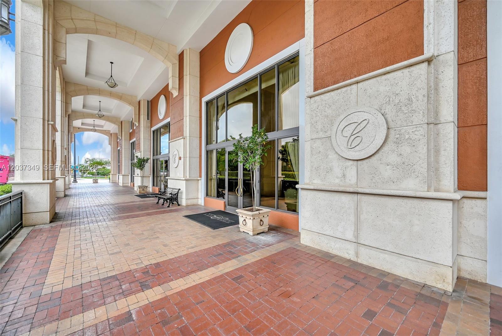 A covered brick walkway leads to the glass entrance of a building with stone accents — 8390 SW 72nd Ave # 905, Miami FL 33143, MIAMI, FL