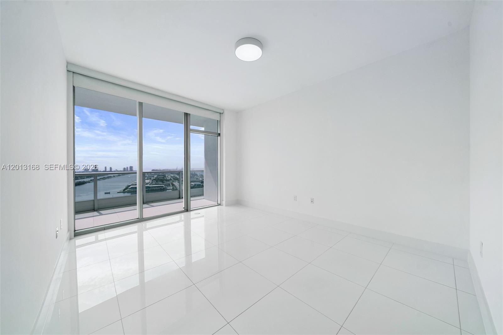An empty room features white tile flooring, plain walls, and a sliding glass door balcony — 900 Biscayne Blvd # 4006, Miami FL 33132, MIAMI, FL