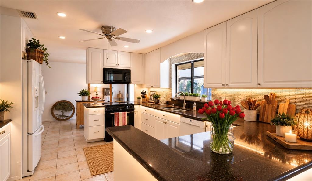 A kitchen features white cabinets, dark granite countertops, a black stove, and a red tulip bouquet — 55 BAY HARBOUR DRIVE, PONCE INLET, FL