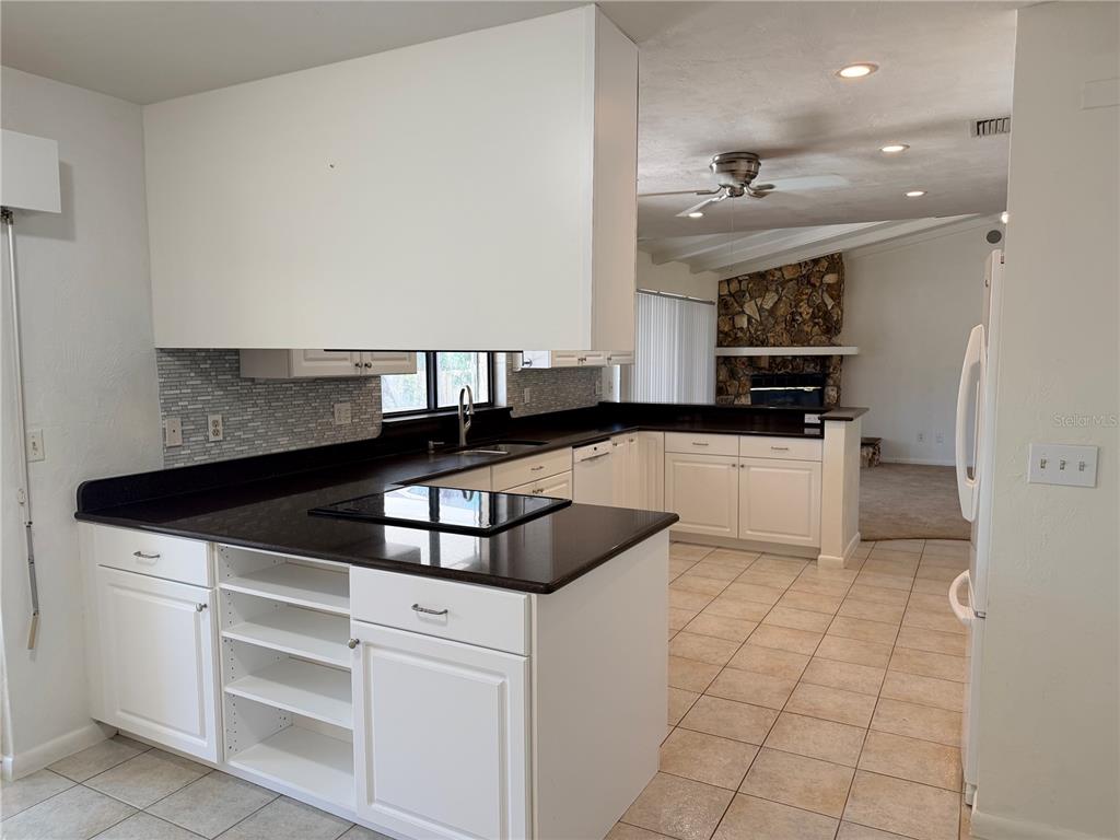 A kitchen with white cabinets, black countertops, and tile flooring overlooks a living room area — 55 BAY HARBOUR DRIVE, PONCE INLET, FL