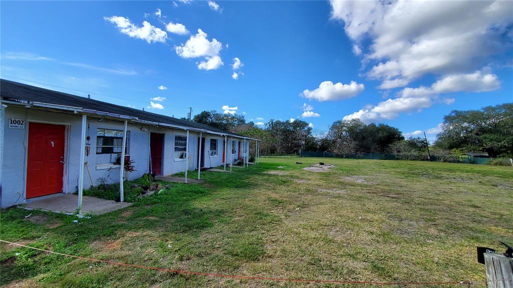 A single-story multi-unit building with red doors sits beside a large, open grassy lot — 1002 DANIELS STREET, DUNDEE, FL