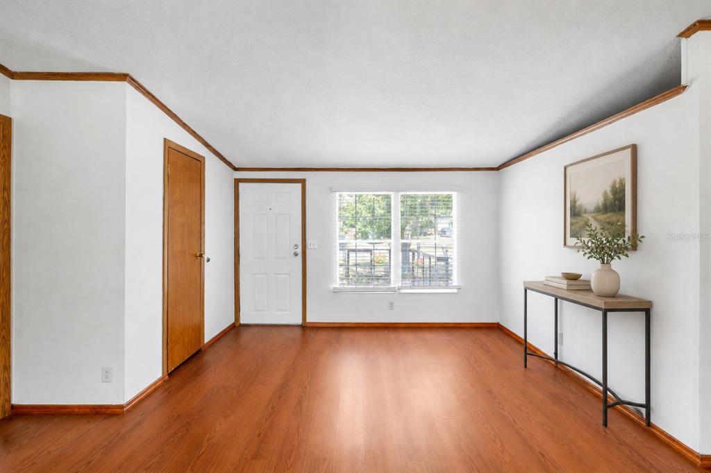 A bright, empty room features wood-look flooring, white walls, a wooden door, and a console table — 12507 ICEWOOD COURT, RIVERVIEW, FL