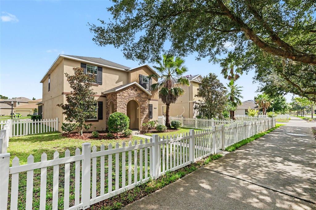 A two-story tan house with a stone entryway and white picket fence on a street — 21087 PLEASANT PLAINS PARKWAY, LAND O LAKES, FL