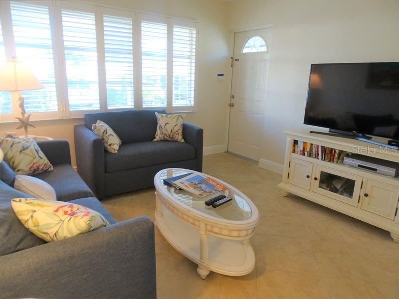 A living room features blue sofas, a glass-topped coffee table, and a white media console — 6020 MIDNIGHT PASS ROAD UNIT 3, SARASOTA, FL