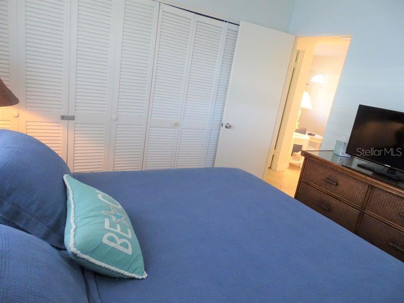A bedroom features a blue bed, a dresser with a television, and louvered closet doors — 6020 MIDNIGHT PASS ROAD UNIT 3, SARASOTA, FL