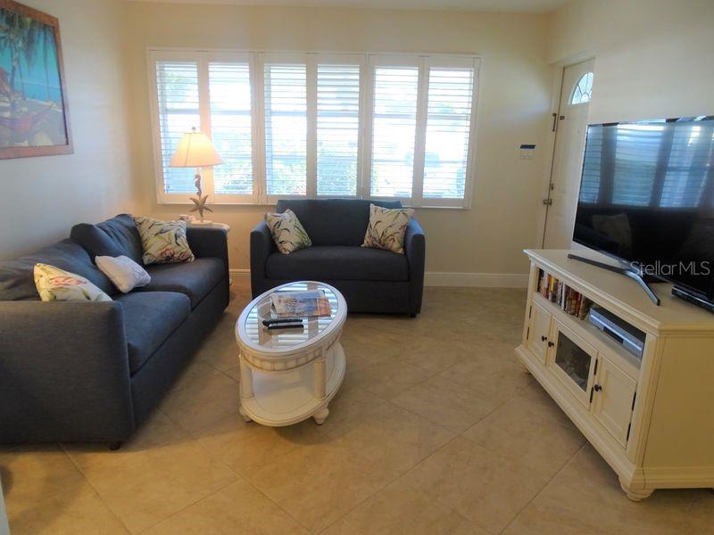 A living room features two blue sofas, a glass-topped coffee table, and a white media console — 6020 MIDNIGHT PASS ROAD UNIT 3, SARASOTA, FL