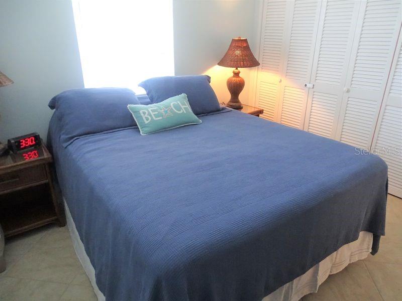 A bedroom features a blue bedspread, a beach-themed pillow, and a bedside lamp — 6020 MIDNIGHT PASS ROAD UNIT 3, SARASOTA, FL