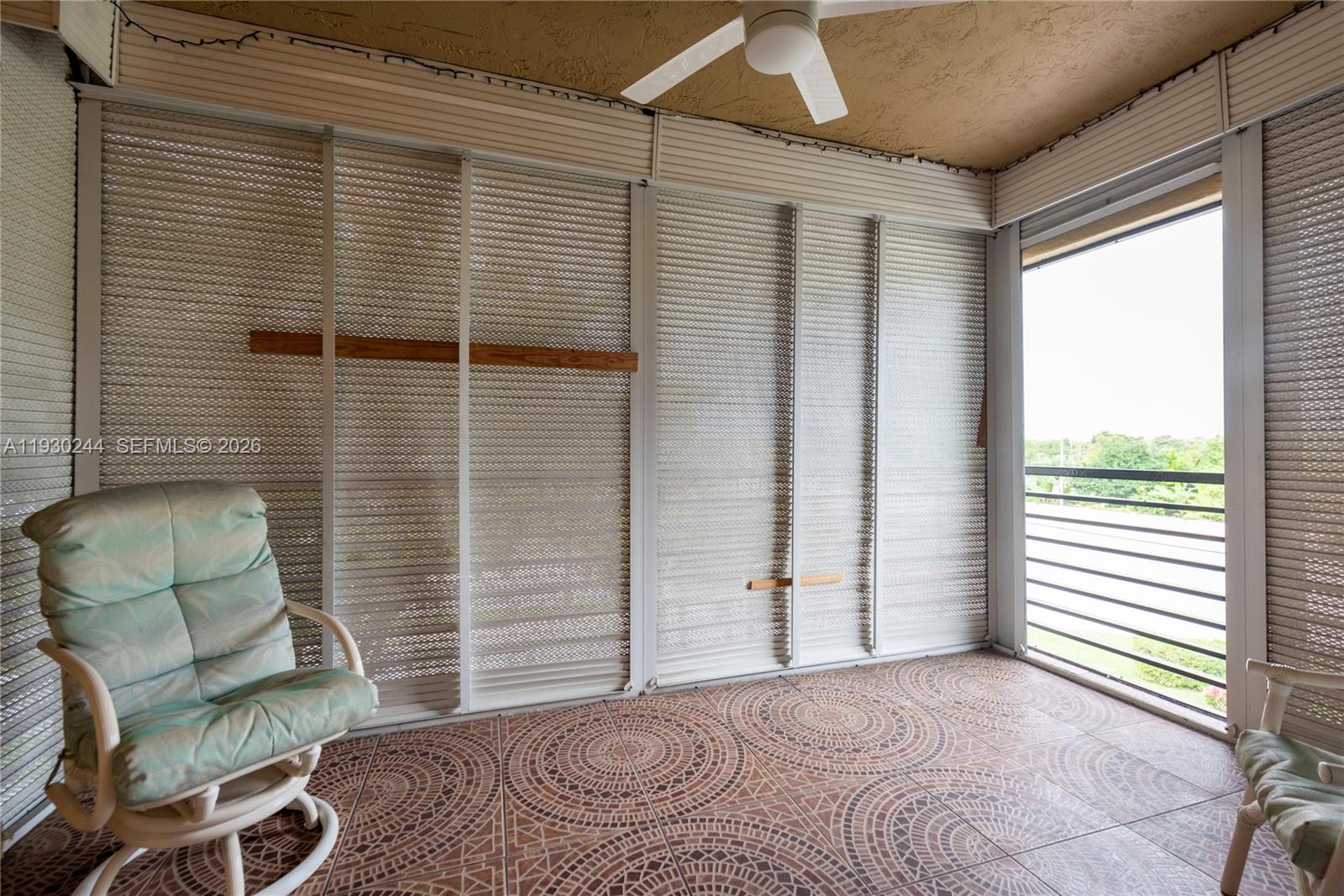 A screened-in balcony features patterned tile flooring, a ceiling fan, and metal storm shutters — 4940 E Sabal Palm Blvd # 414, Tamarac FL 33319, TAMARAC, FL