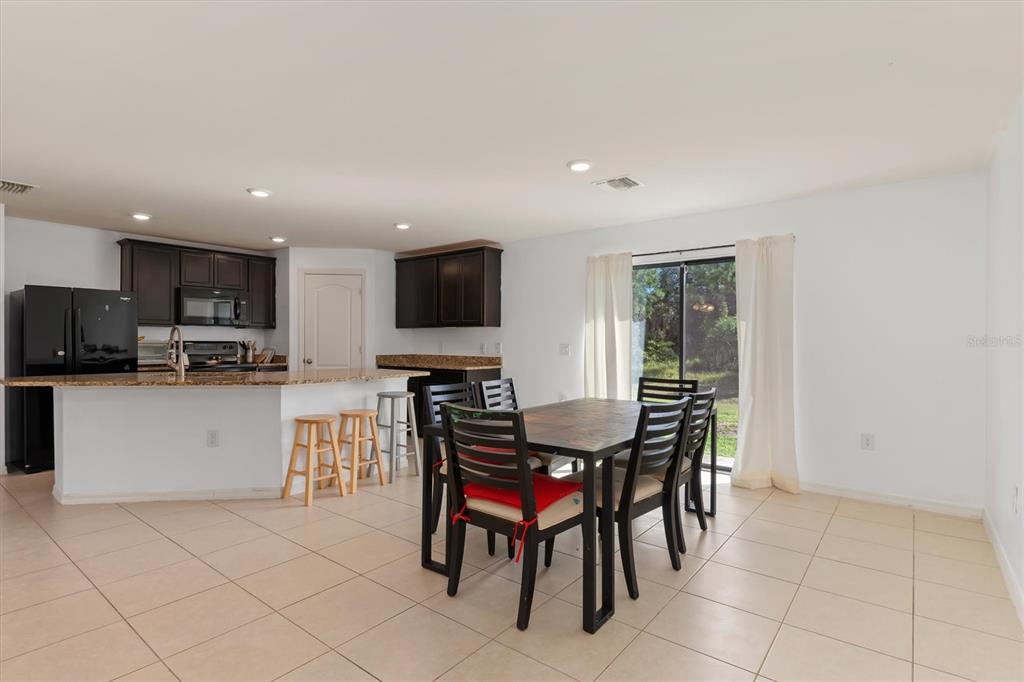 An open-concept kitchen and dining area with dark cabinets, granite countertops, and tile flooring — 4234 GALVIN LANE, NORTH PORT, FL