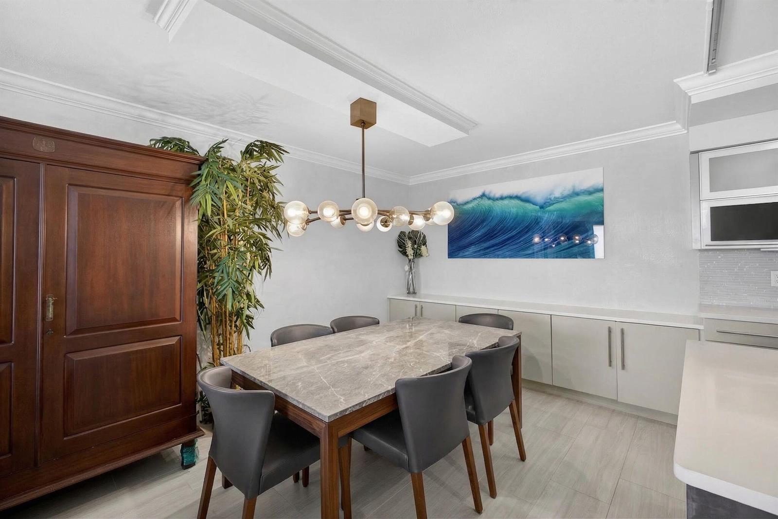 A dining room features a marble-topped table, grey chairs, a modern chandelier, and wall art — 5440 N Ocean Drive # 805, Singer Island FL 33404, SINGER ISLAND, FL