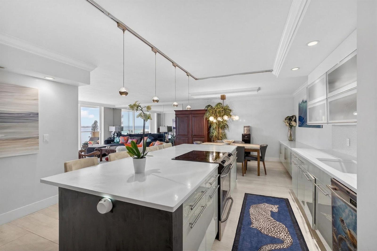A modern kitchen with a white island and stainless steel appliances opens to a living area — 5440 N Ocean Drive # 805, Singer Island FL 33404, SINGER ISLAND, FL