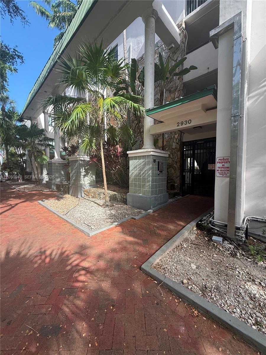 An exterior view of a building entrance with brick walkways, palm trees, and stone accents — 2924 Day Ave # N110, Miami FL 33133, MIAMI, FL
