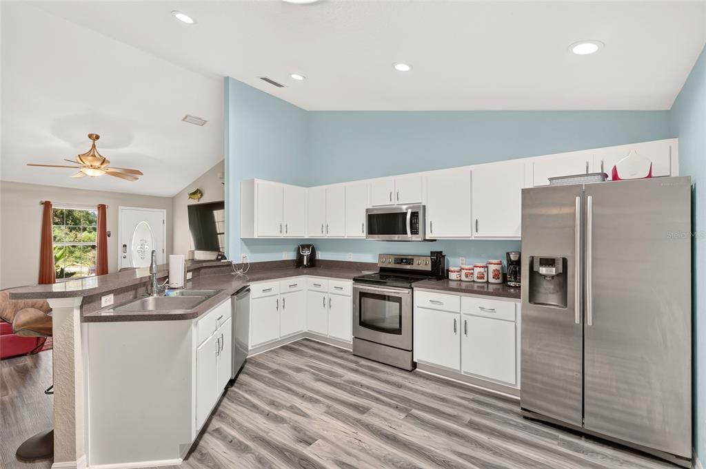 A kitchen features white cabinets, stainless steel appliances, dark countertops, and light wood-look flooring — 6 OAK CIRCLE COURSE, OCALA, FL