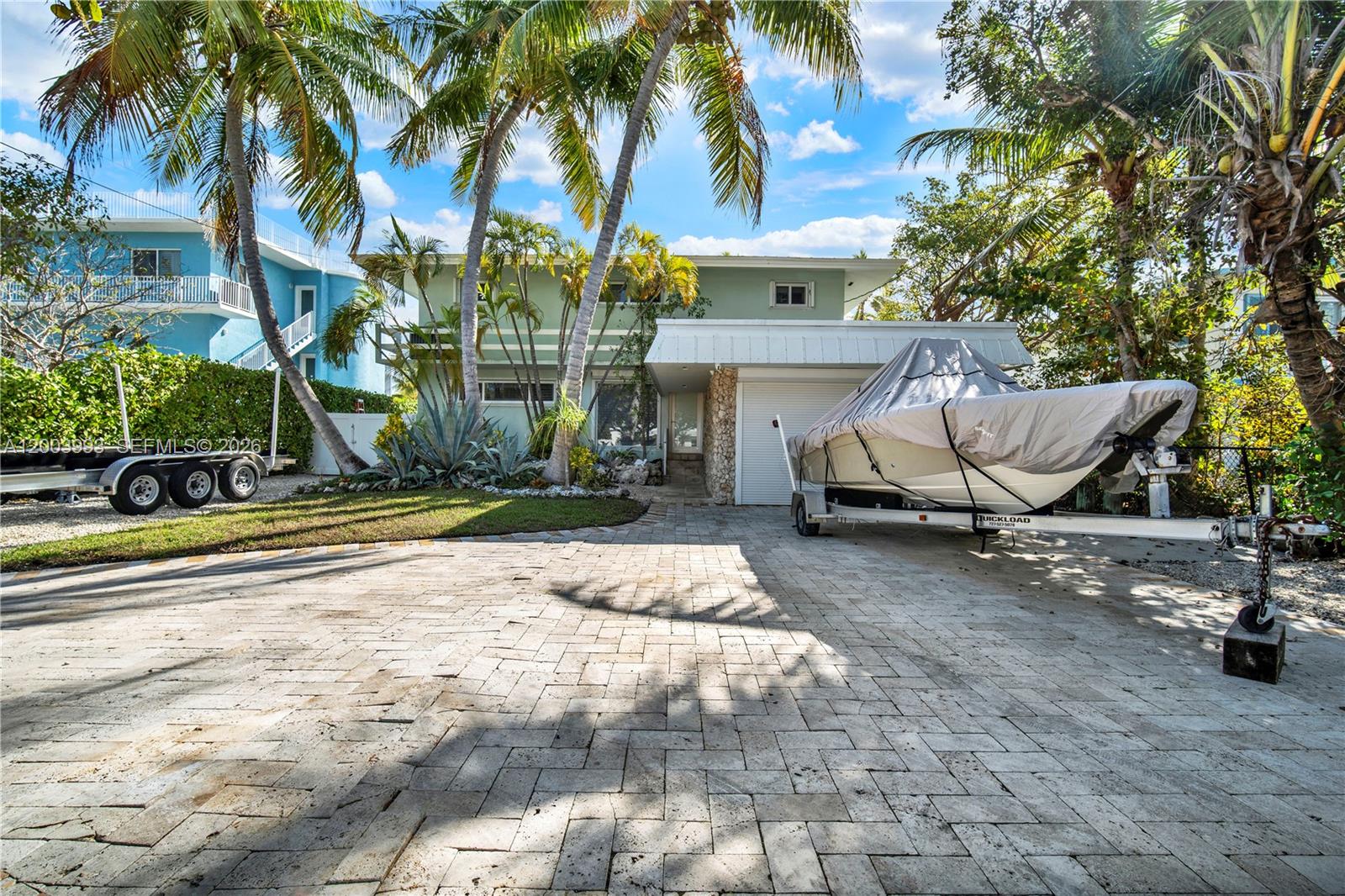 A two-story house with a paved driveway, palm trees, and a boat on a trailer — 69 Shoreland Dr, Key Largo FL 33037, KEY LARGO, FL