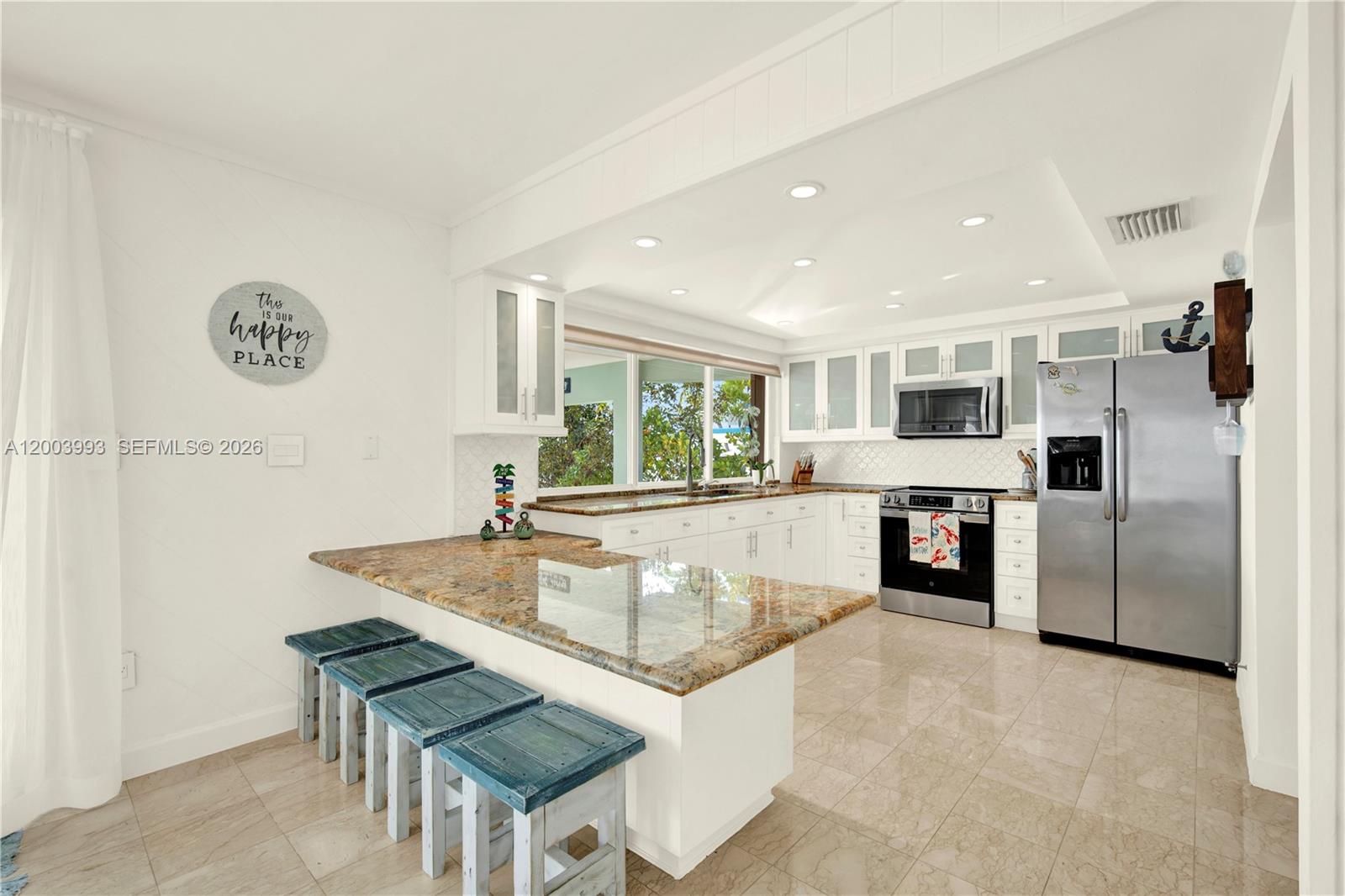 A kitchen features white cabinetry, granite countertops, a breakfast bar, and stainless steel appliances — 69 Shoreland Dr, Key Largo FL 33037, KEY LARGO, FL