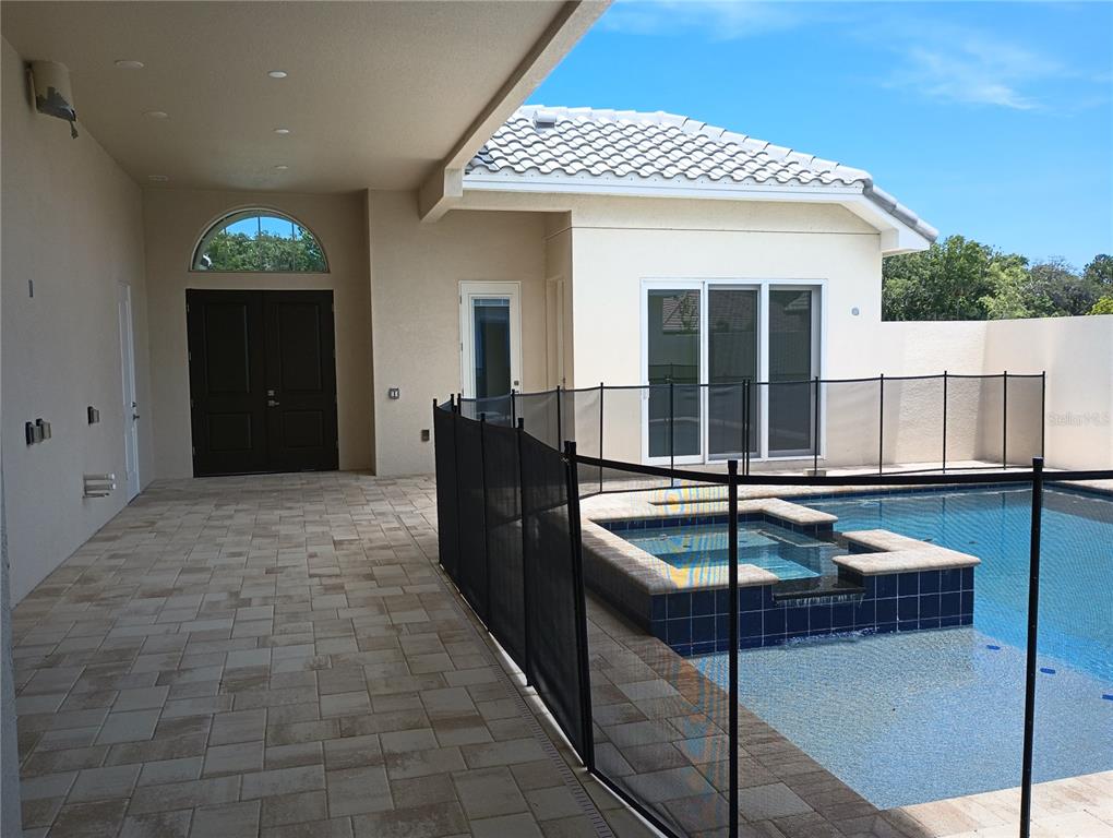 A covered patio features light-colored pavers, a dark double door, and a fenced swimming pool — 136 NEW LEATHERWOOD DRIVE, PALM COAST, FL