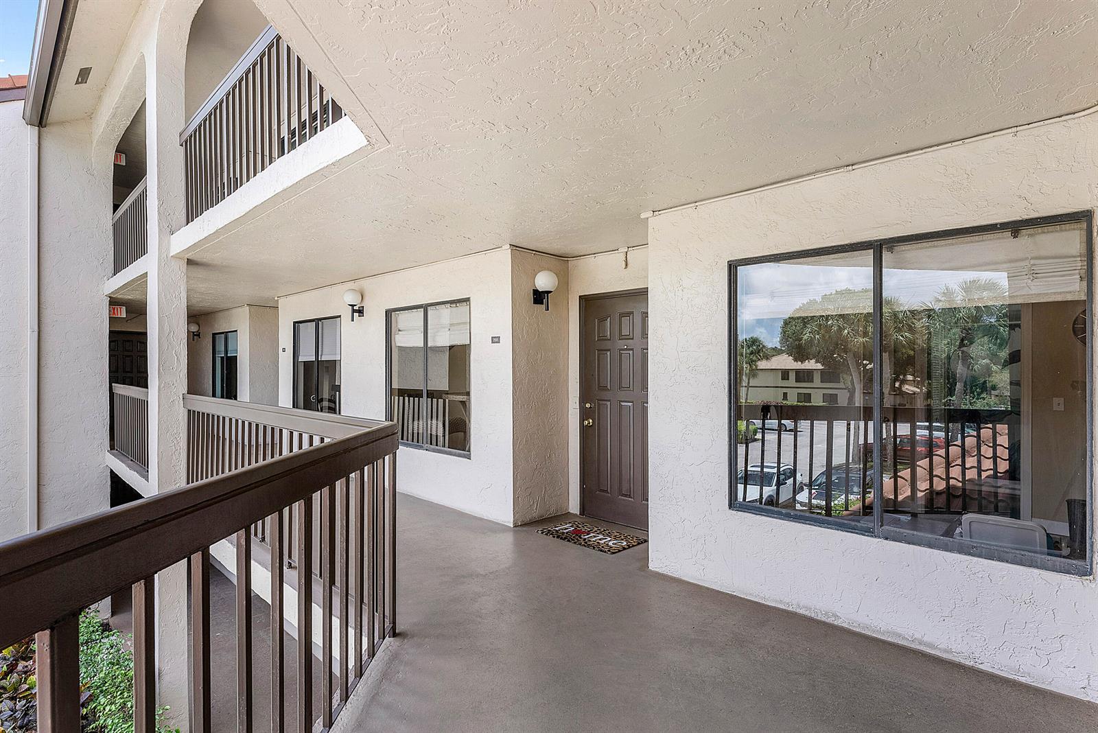 An exterior walkway features a brown door, large windows, and a metal railing — 10110 Cedar Point Boulevard # 203, Boynton Beach FL 33437, BOYNTON BEACH, FL