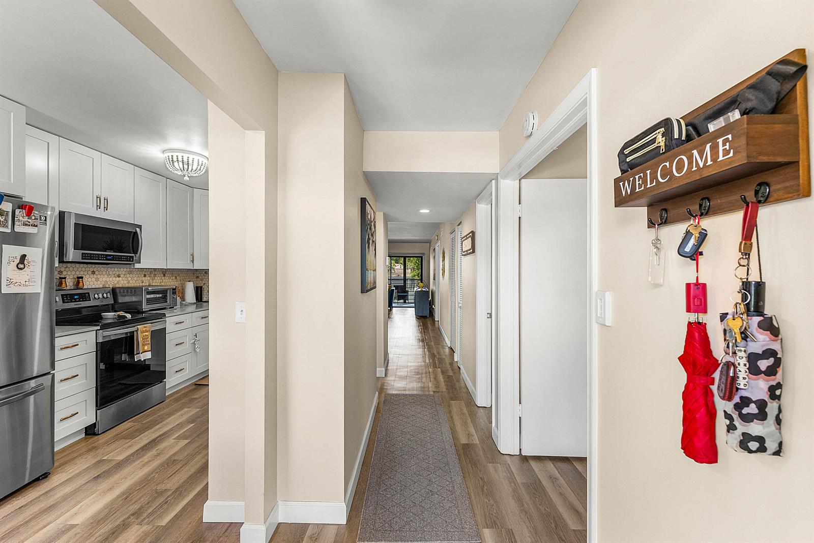 A hallway with wood-look flooring leads past a white kitchen to a distant living area — 10110 Cedar Point Boulevard # 203, Boynton Beach FL 33437, BOYNTON BEACH, FL