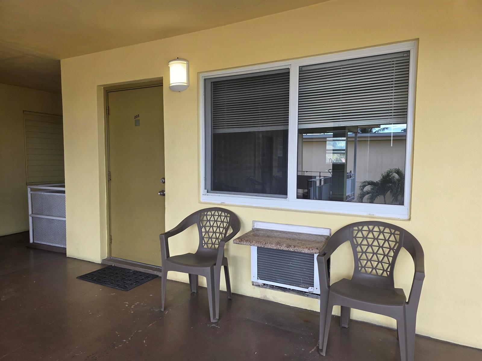 A yellow exterior wall features a door labeled 205, a window with blinds, and two chairs — 911 N Federal Highway # 205, FL 33460, FL