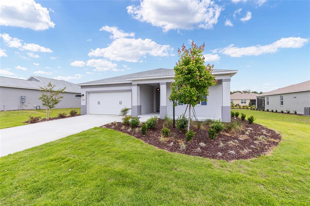 A single-story house with a white garage, gray exterior, and a landscaped front yard — 10323 SW 105TH TERRACE, OCALA, FL