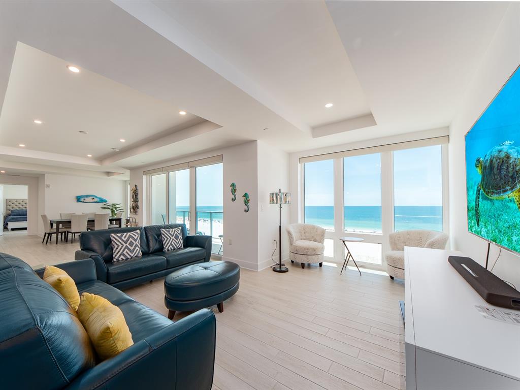 A living room with blue leather sofas, light wood floors, and floor-to-ceiling ocean views — 15 AVALON STREET UNIT 701, CLEARWATER BEACH, FL