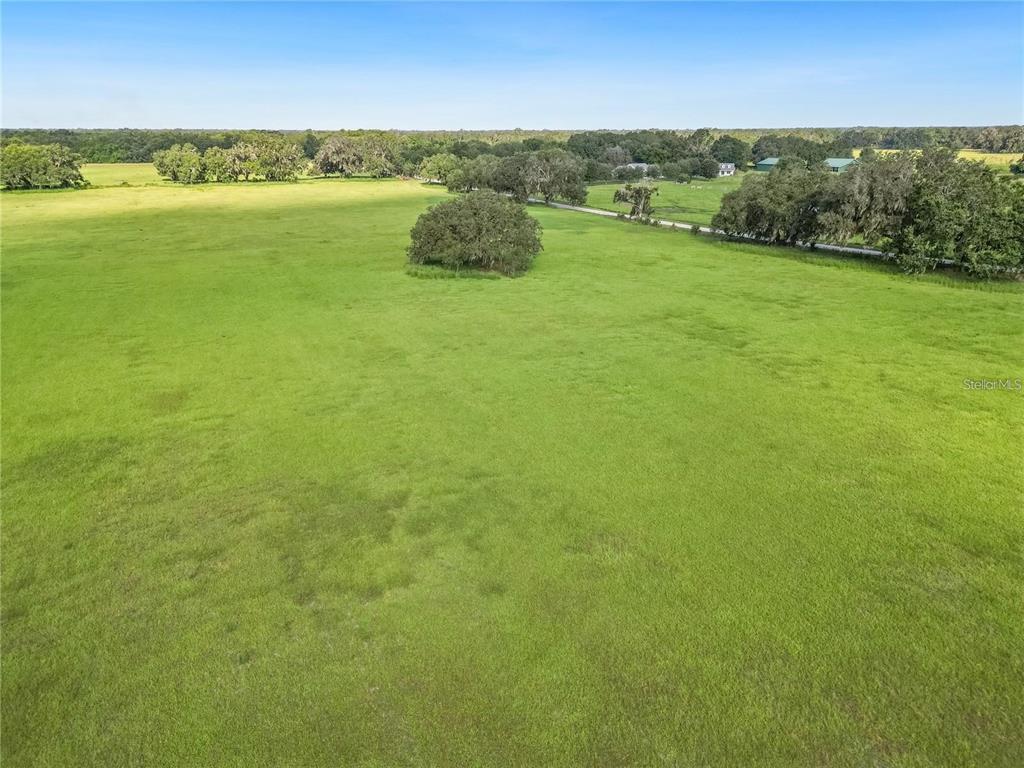 An aerial view shows a large, open green pasture with scattered trees and a dirt road — 5780 CR 569, CENTER HILL, FL