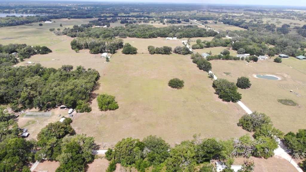 An aerial view shows a large, open grassy field surrounded by trees and rural properties — 5780 CR 569, CENTER HILL, FL