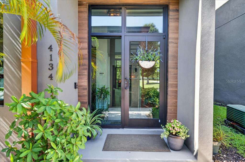 The exterior entrance of a modern home features a glass door, palm trees, and landscaping — 4134 GAUGE LINE LOOP, TAMPA, FL