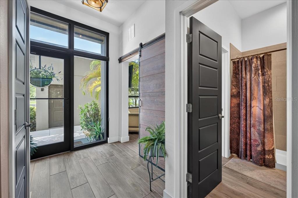 A hallway with wood-look tile flooring leads to a glass front door and a bathroom — 4134 GAUGE LINE LOOP, TAMPA, FL
