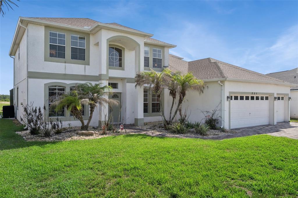 A two-story stucco house with a three-car garage and palm trees in the front yard — 231 BELFRY DRIVE, DAVENPORT, FL