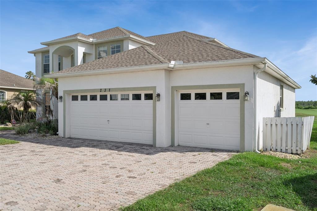 A two-story house with a three-car garage and a paved driveway under a blue sky — 231 BELFRY DRIVE, DAVENPORT, FL