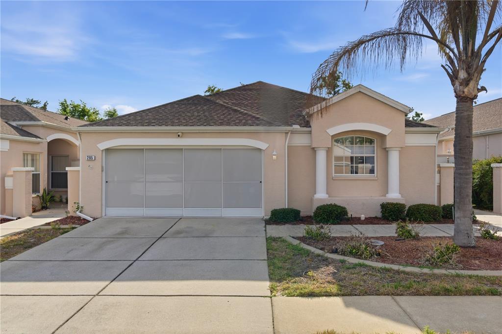 A single-story house with a beige stucco exterior, a screened garage door, and a palm tree — 295 ROYAL PALM WAY, SPRING HILL, FL