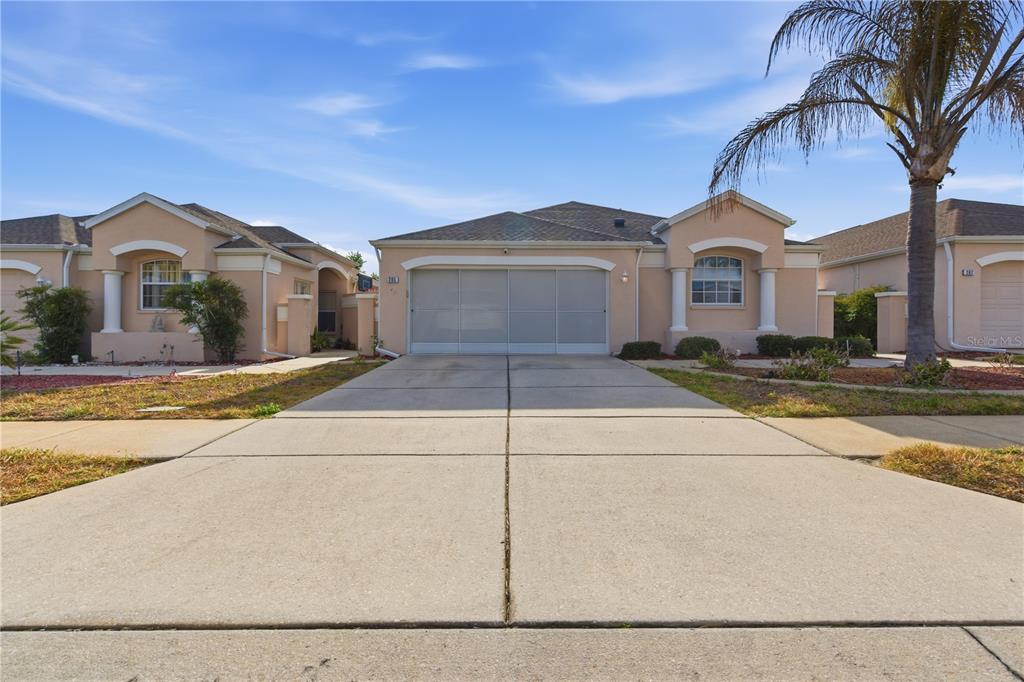 A single-story house with a beige stucco exterior, a two-car garage, and a concrete driveway — 295 ROYAL PALM WAY, SPRING HILL, FL