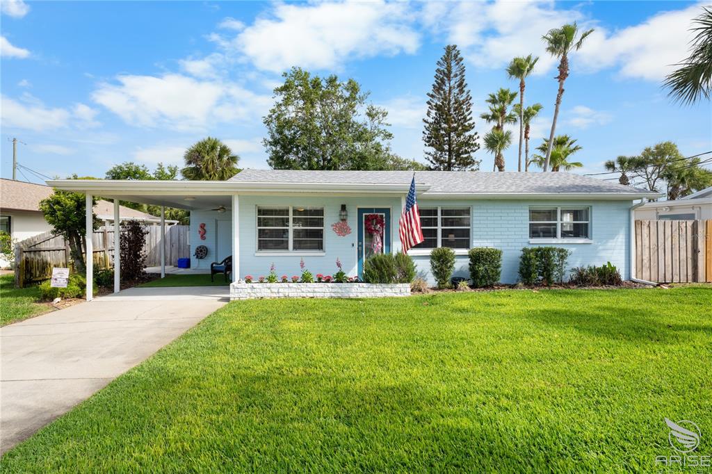 A light blue single-story house with a carport, front lawn, and an American flag — 702 OCEAN AVENUE, NEW SMYRNA BEACH, FL