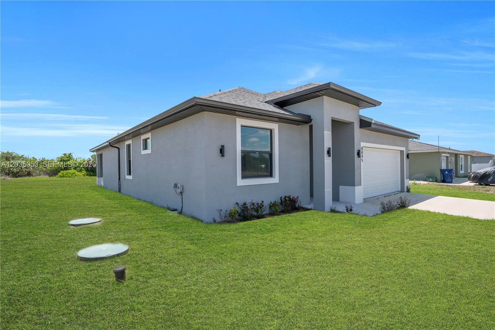 A gray single-story house with a white garage door sits on a grassy lot — 8045 Buttercup Cir, La Belle FL 33935, LA BELLE, FL