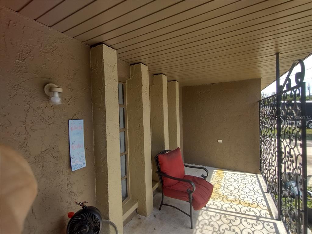 A covered front porch features a red chair, a decorative metal railing, and a wall sign — 2419 APPIAN AVENUE, SPRING HILL, FL