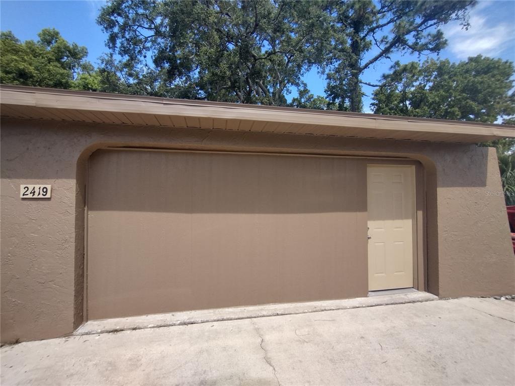 A brown exterior wall features a large garage door and a single adjacent entry door — 2419 APPIAN AVENUE, SPRING HILL, FL
