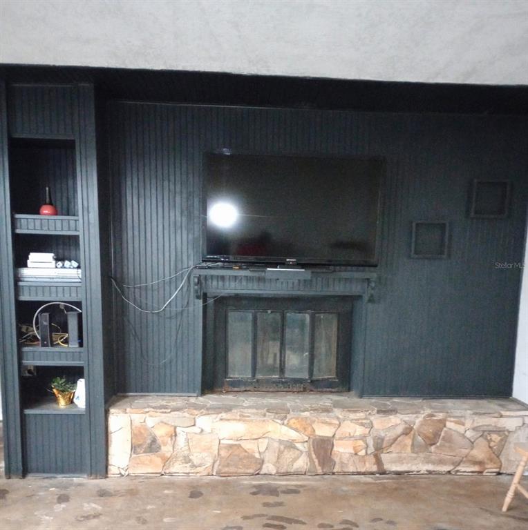 A dark-painted fireplace wall features a mounted television, built-in shelving, and a stone hearth — 2419 APPIAN AVENUE, SPRING HILL, FL