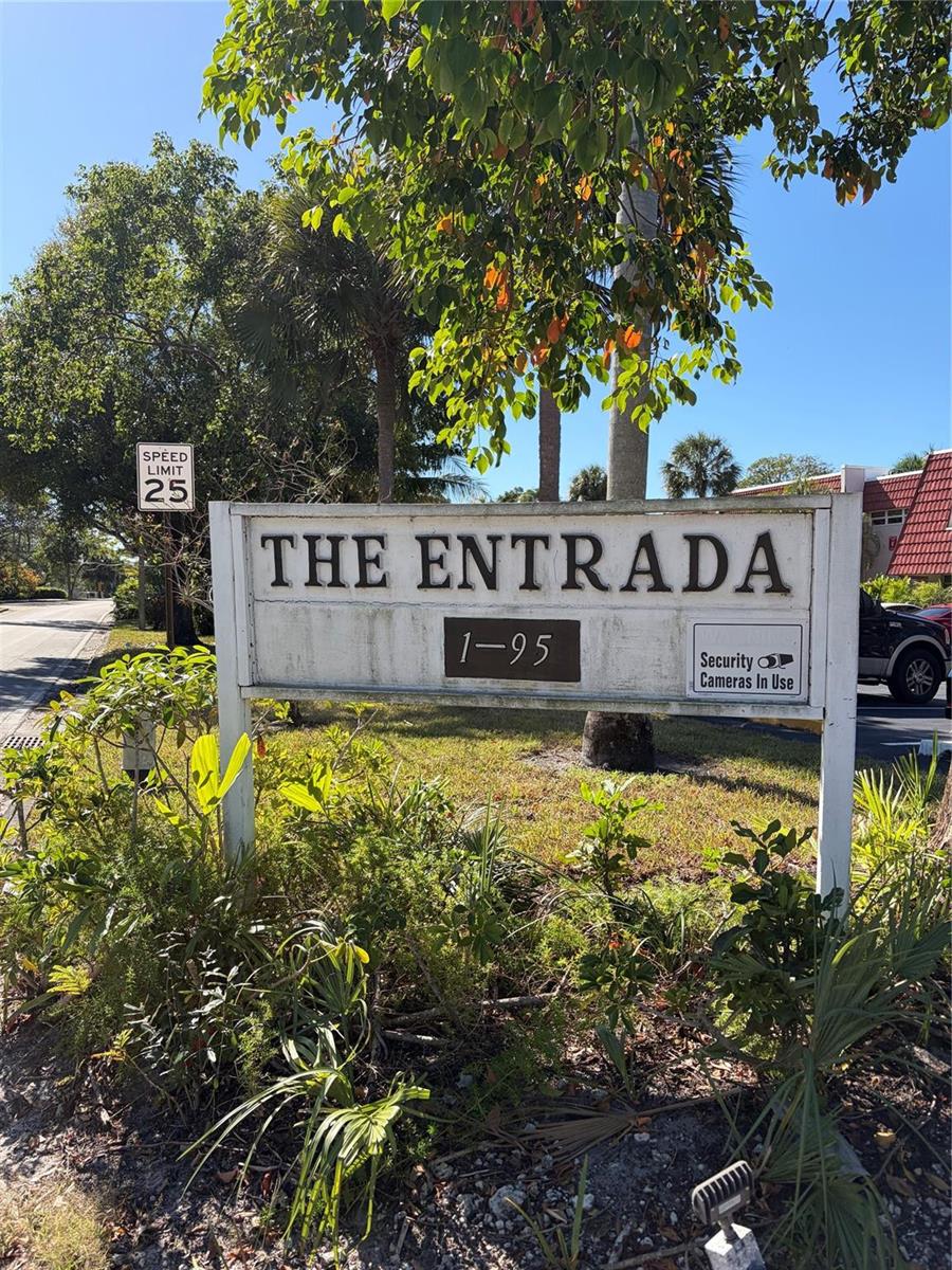 A weathered sign for The Entrada stands in front of trees and a speed limit sign — 21 Jacaranda Drive # 121, Plantation FL 33324, PLANTATION, FL