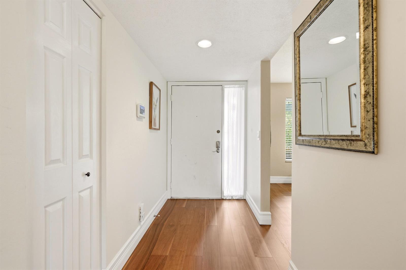 An entryway features a white front door, wood flooring, a closet, and a wall mirror — 5500 Fairway Park Drive # 103, Boynton Beach FL 33437, BOYNTON BEACH, FL