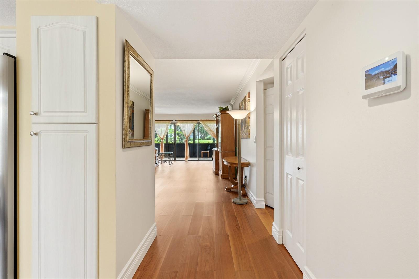 A hallway with wood flooring leads to a living area with sliding glass doors — 5500 Fairway Park Drive # 103, Boynton Beach FL 33437, BOYNTON BEACH, FL