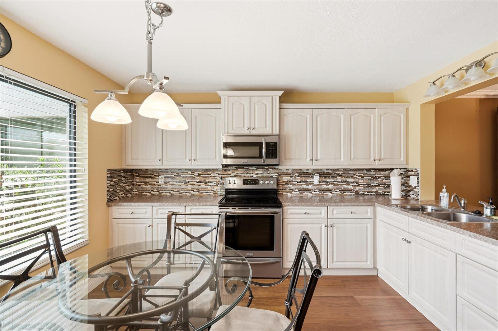 A kitchen features white cabinets, stainless steel appliances, a mosaic backsplash, and a glass-topped table — 5500 Fairway Park Drive # 103, Boynton Beach FL 33437, BOYNTON BEACH, FL