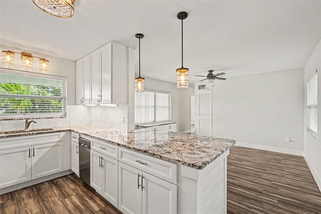 A kitchen features white cabinets, granite countertops, a breakfast bar, and wood-look tile flooring — 2009 TARPON ROAD, PALMETTO, FL