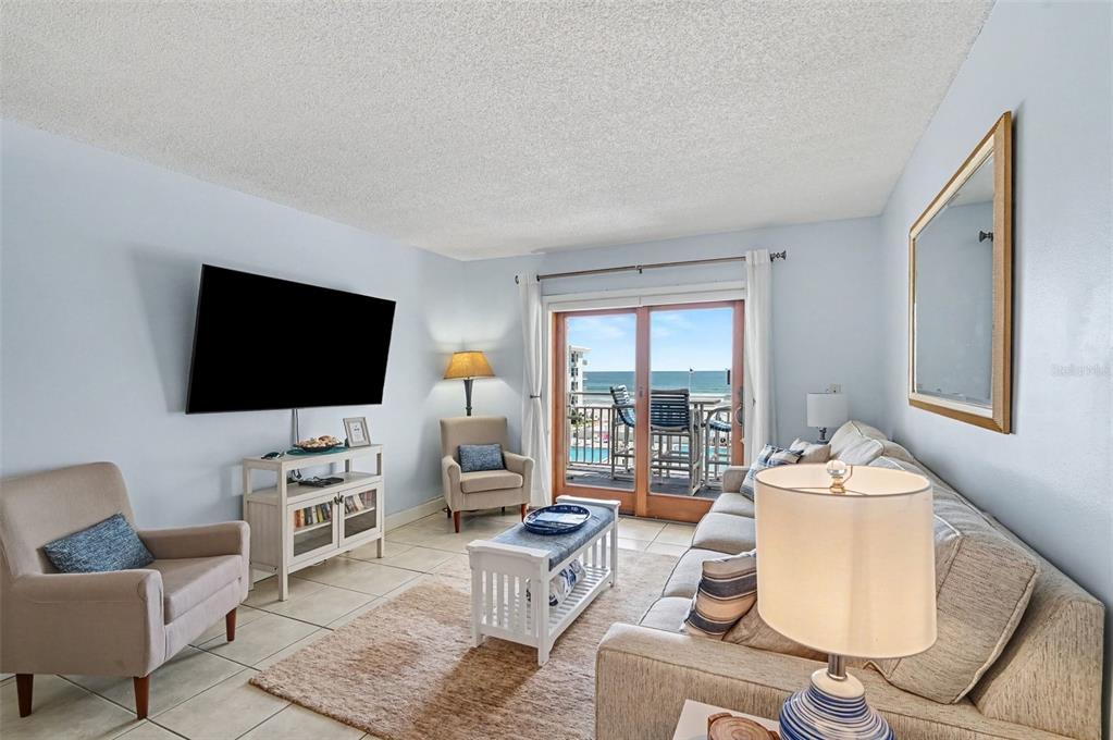 A living room features a sofa, armchairs, a television, and a balcony overlooking the ocean — 4153 S ATLANTIC AVENUE UNIT 4160, NEW SMYRNA BEACH, FL
