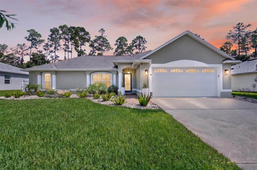A single-story house with a two-car garage, light-colored stucco exterior, and a landscaped front yard — 98 WESTGRILL DRIVE, PALM COAST, FL